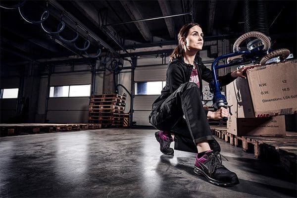 Eine Dame die in einer Logistikhalle am arbeiten ist und Sicherheitsschuhe mit Stahlkappen trägt. In pink und schwarz.