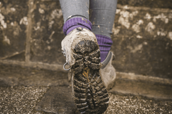 Dreckige Schuhsohlen eines Sicherheitsschuh, werden von einer Frau mit violetten Socken getragen.