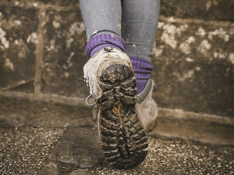 Dreckige Schuhsohlen eines Sicherheitsschuh, werden von einer Frau mit violetten Socken getragen.