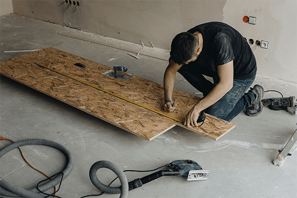 Ein Handwerker zeichnet mit einem Meter Abmessungen auf einer Spanplatte ein