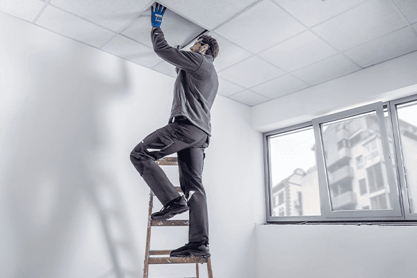 Ein Arbeiter trägt ergonomische Arbeitsschuhe, bei der Arbeit auf einer Leiter, in einem leeren, noch Trockenbau-Raum