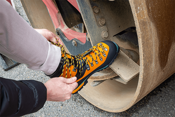 Ein Arbeiter bindet einen orangefarbenen Sicherheitsschuh. Ein teurer Arbeitsschuh aus hochwertigen Materialien.